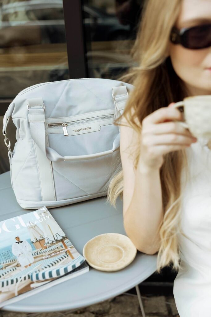 Kobieta pijąca kawę, na stoliku torba podróżna