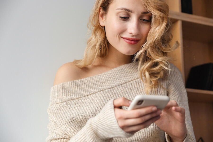 Kobieta o blond włosach czytająca z zaciekawieniem wiadomość z telefonu