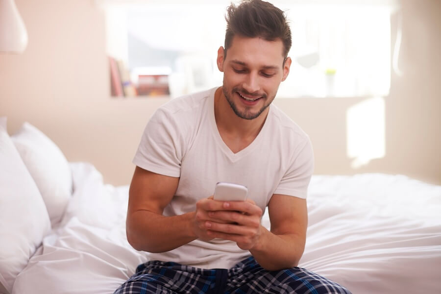 Mężczyzna siedzący na łóżku podczas pisania wiadomości na telefonie do kobiety