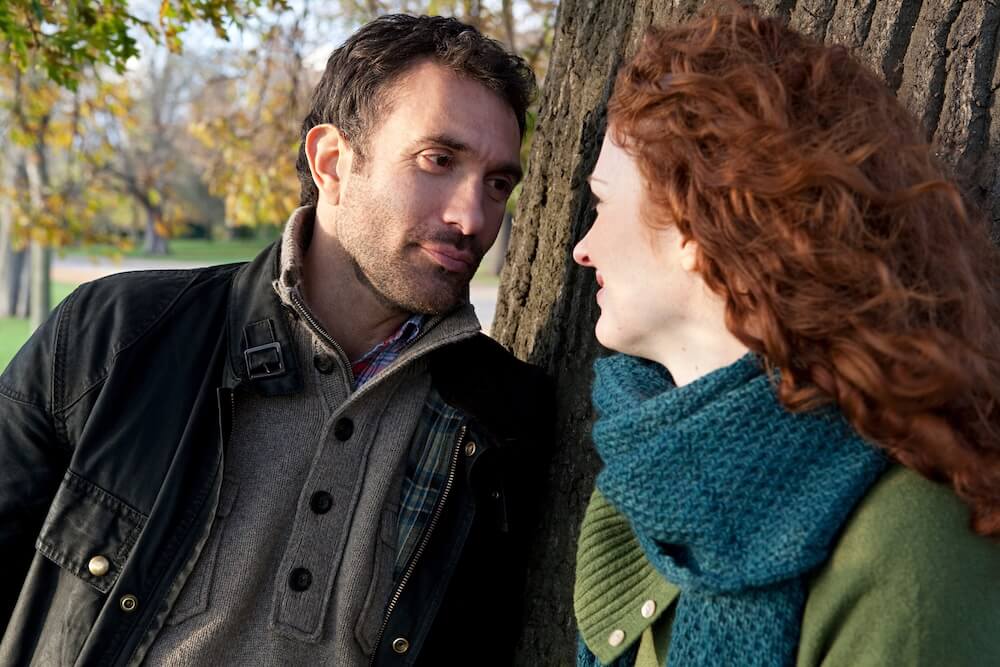 Miły mężczyzna skracający dystans do kobiety o rudych włosach przy drzewie