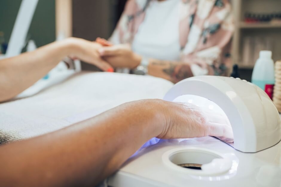 Kobieta trzymający dłoń pod lampą do utrwalania manicure