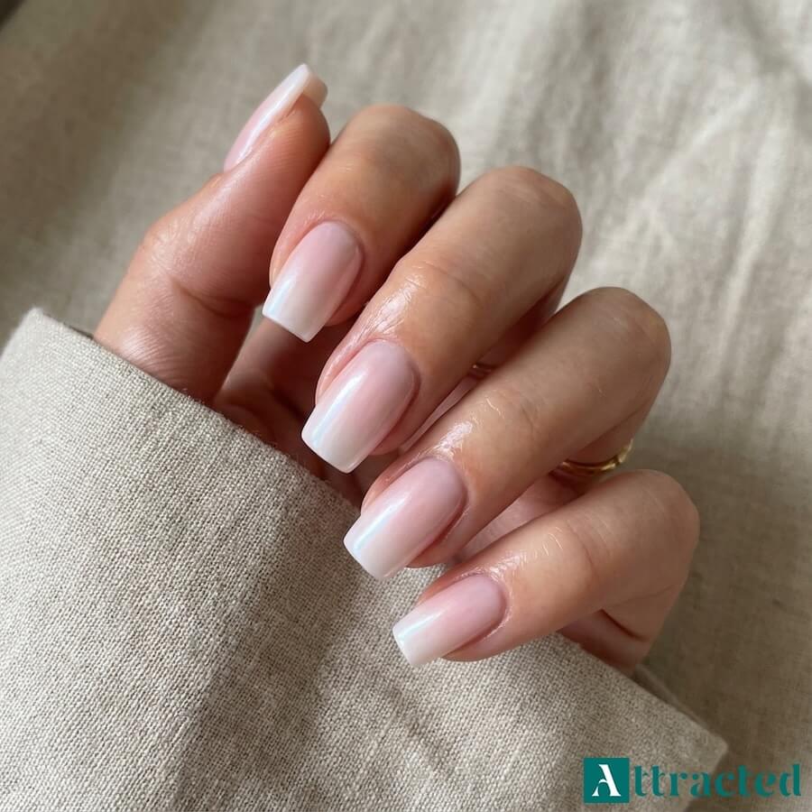 Zbliżenie jednej dłoni z migdałkowymi paznokciami baby boomer z opalizującym pyłkiem w różowo-liliowych tonach, na jasnym neutralnym tle