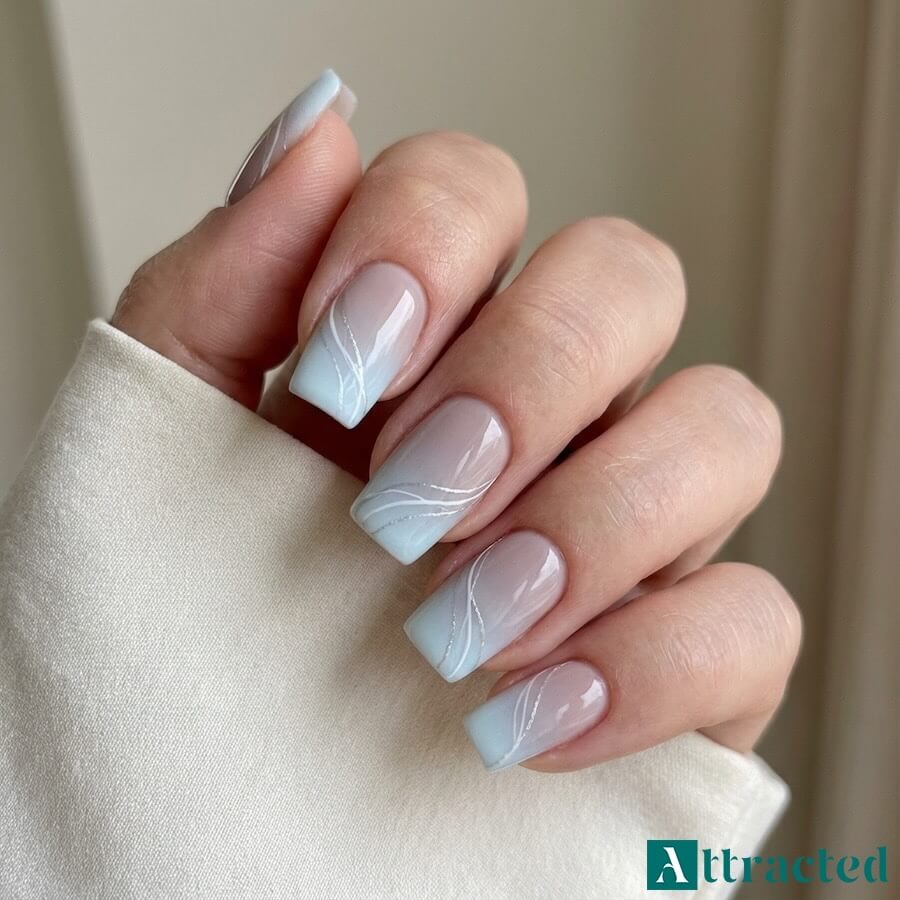 Zbliżenie jednej dłoni z kwadratowymi paznokciami ombre french nude do chłodnego błękitu z białymi i srebrnymi zawijasami, na jasnym neutralnym tle