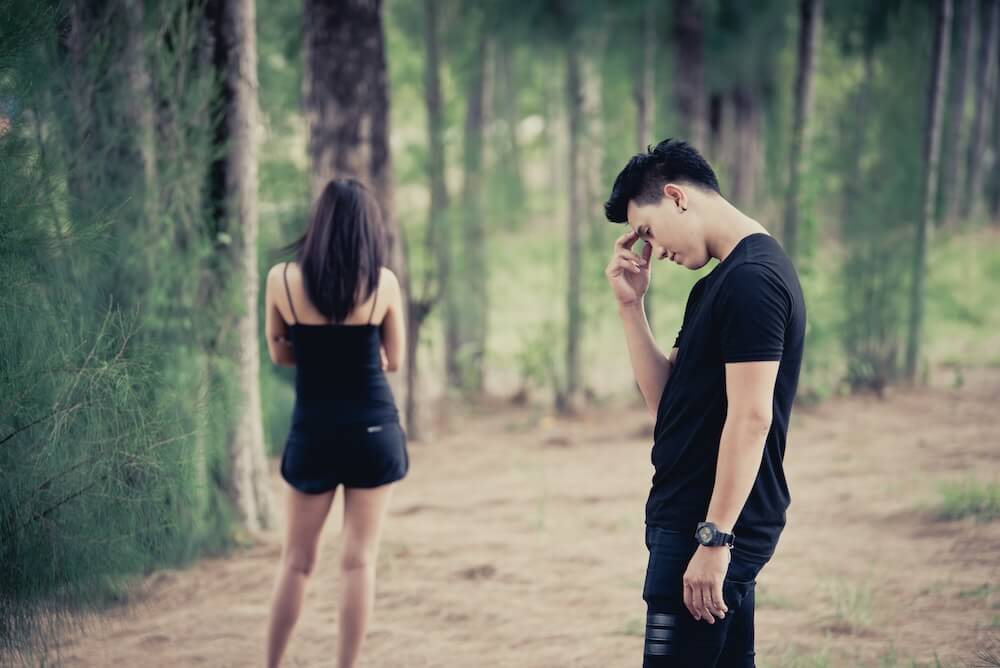 Załamany mężczyzna ubrany na czarno i kobieta w oddali ubrana na czarno w lesie