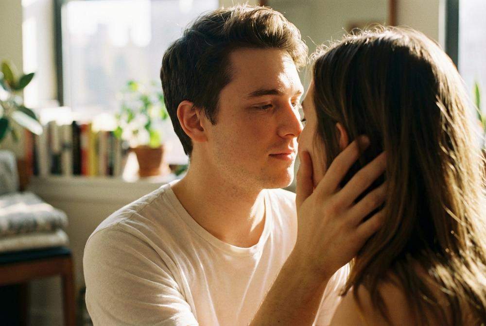 Mężczyzna czule trzyma twarz kobiety w dłoniach przed pocałunkiem